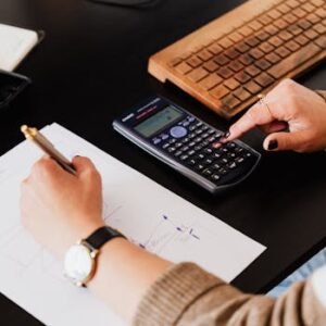 Close-up of hands working with a calculator and notebook on a desk, analyzing documents.