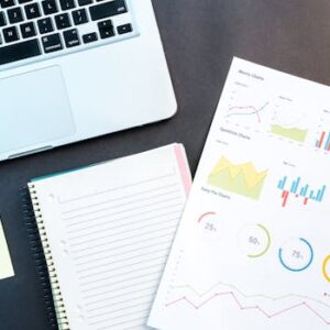 Flatlay of business report with colorful charts, a notebook, and a laptop for data analysis on a desk.