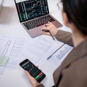 A business professional analyzing stock charts on a laptop and smartphone at the office.